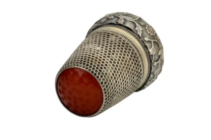 Hier sehen Sie einen silbernen Fingerhut mit einem roten Glasaufsatz und Blumen am unteren Rand.  Der Fingerhut ist ca 2,7 cm hoch und hat einen Durchmesser von 1,9 cm. Er wiegt 5,8 g und ist in einem sehr guten gebrauchten Zustand.